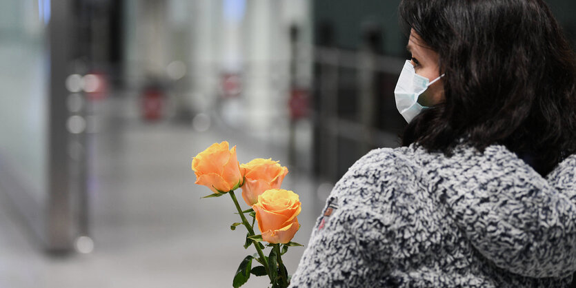 Eine Frau trägt einen Mundschutz und hält drei Rosen in der Hand