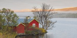 Ein rotes Holzhaus steht an einem See in Norwegen