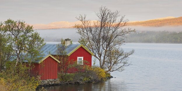 Ein rotes Holzhaus steht an einem See in Norwegen