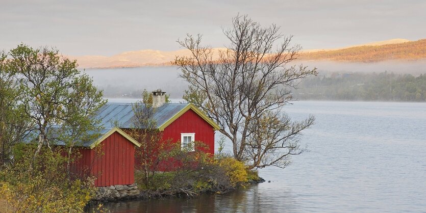 Ein rotes Holzhaus steht an einem See in Norwegen