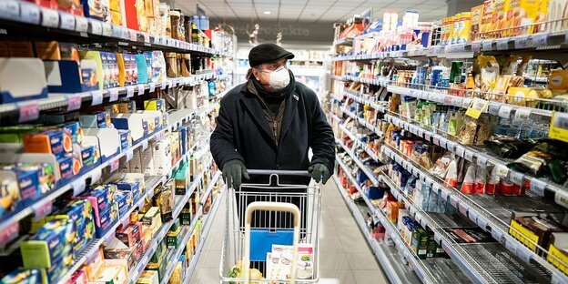 Ein Mann mit Mundschutz sciebt einen Einkaufswagen durch einen Supermarkt