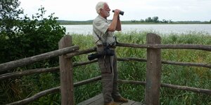 Mit dem Fernglas in der Hand an einem See stehend: Brandenburgs Storchenexperte Bernd Ludwig hält Ausschau nach seinen Lieblingstieren
