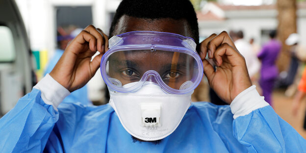 Ein Mann setzt eine Schutzbrille auf und trägt eine Atemschutzmaske