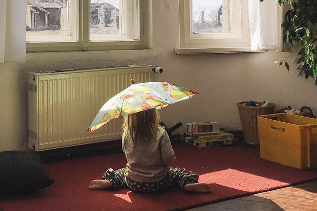 Ein Kind sitzt unter einem Regenschirm im Wohnzimmer