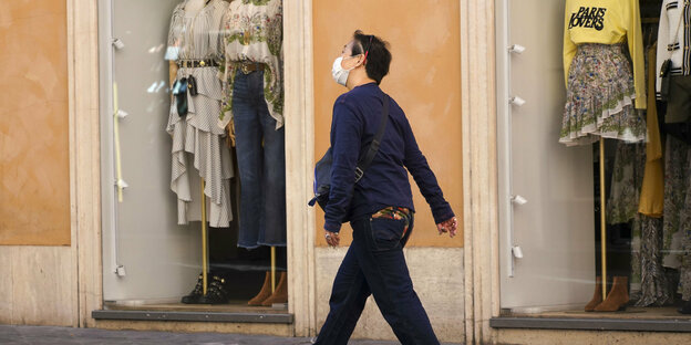 Mann mit Maske geht vor Schaufenstern mit Kleidern entlang