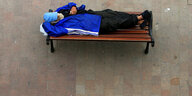 Ein wohnungsloser Mensch schläft auf einer Bank
