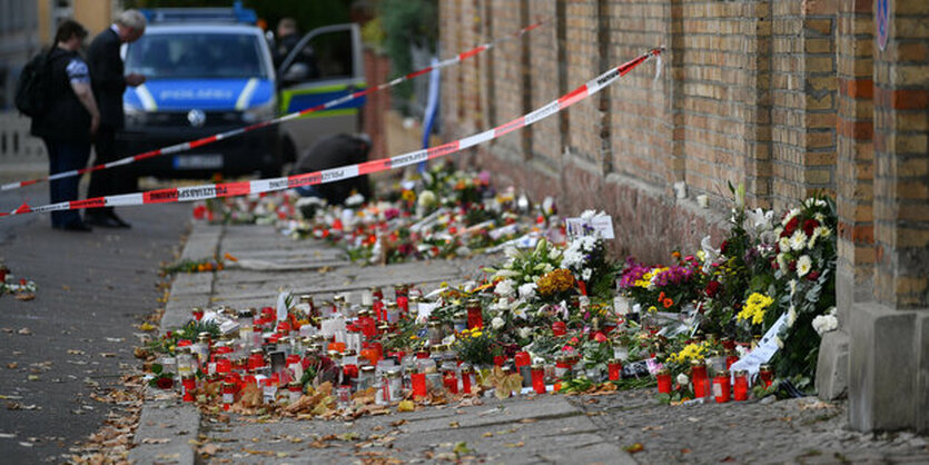 Blumen und Kerzen an einer Mauer, im Hintergrund ein POlizeiauto