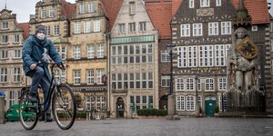 Ein Mann mit Mundschutzmaske fährt auf einem Fahrrad über den leeren Bremer Marktplatz.