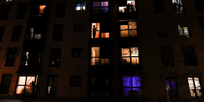 Menschen in der Nacht an ihren erleuchteten Fenstern stehend in einem mehrstöckigem Haus in Madrid