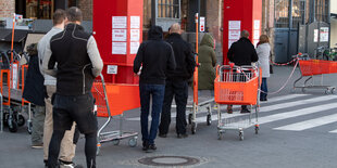 Kunden mit Einkaufswagen und viel Abstand vor einem Baumarkt in Schöneberg