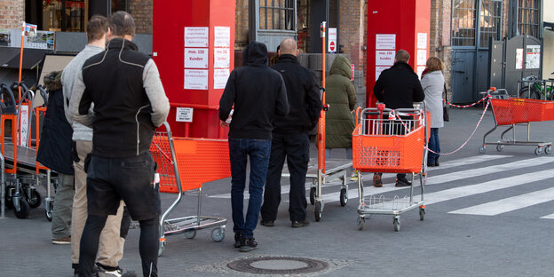 Kunden mit Einkaufswagen und viel Abstand vor einem Baumarkt in Schöneberg