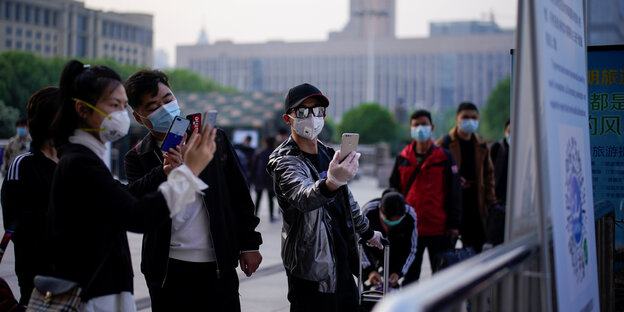 Menschen mit Mundschutz um stehen vor einer Tafel, die sie mit ihren Handys abscannen