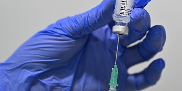 Eine behandschuhte Hand mit Covid-19-Impfstoff beim aufziehen der Spritze