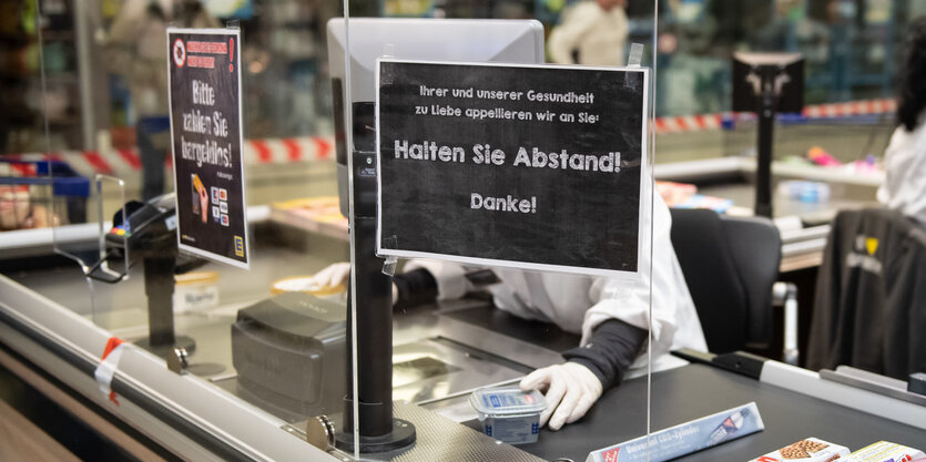 Eine Mitarbeiterin eines Edeka-Marktes sitzt an der Kasse hinter einem Spuckschutz