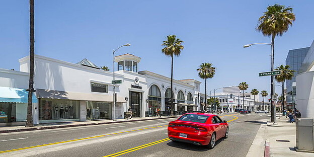 ein Straßenzug in Beverly Hills, mit weißen einstöckigen Häuser, Palmen und einem roten Sportwagen