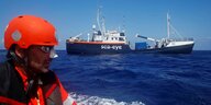 Das Rettungsschiff Alan Kurdi auf dem offenen Meer, im Vordergrund ein Mann mit orangenem Helm und Rettungsweste auf einem Schlauchboot