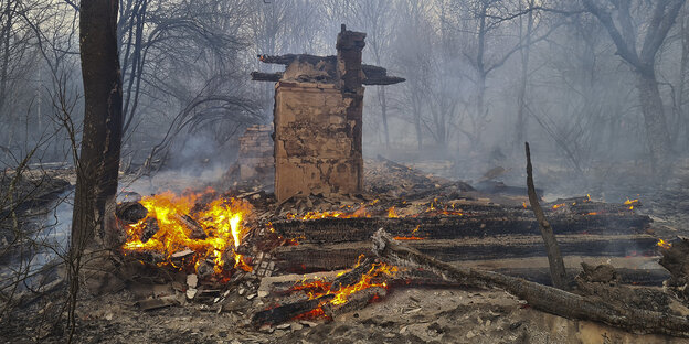 Reste eines abgebrannten Gebäudes im Wald, es lodert noch Feuer im Schutt