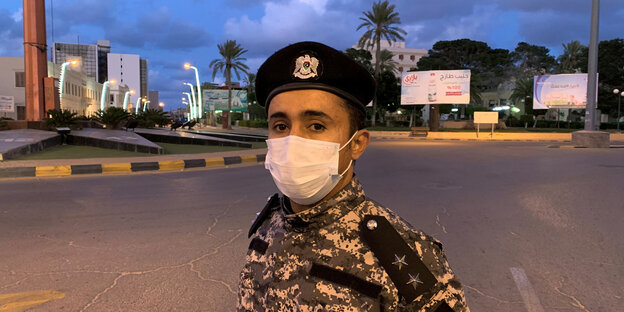 Ein junger Mann in militärischer Uniform trägt einen Mundschutz, im Hintergrund eine leere Straße.