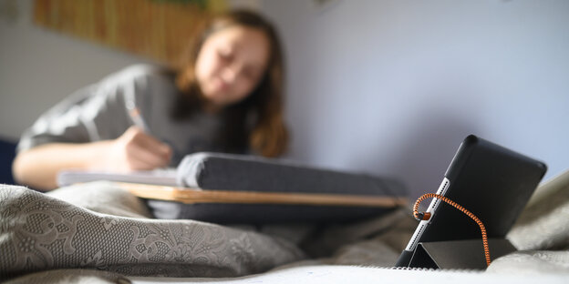 Eine Schülerin arbeitet auf einem Tablet in ihrem Bett für die Schule