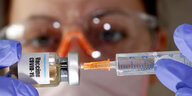 Eine Frau steckt eine Spritze in ein Fläschchen auf dem "Vaccine Covid-19" steht