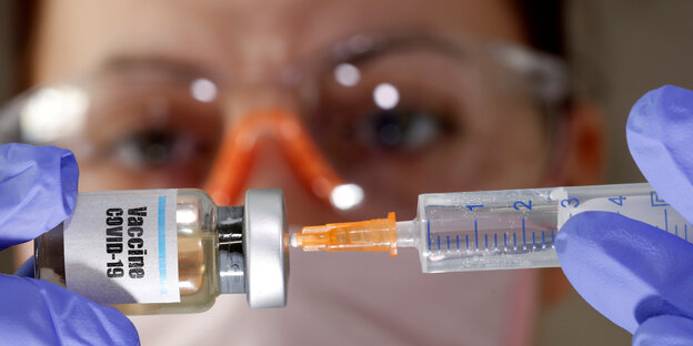 Eine Frau steckt eine Spritze in ein Fläschchen auf dem "Vaccine Covid-19" steht Eine Frau steckt eine Spritze in ein Fläschchen auf dem "Vaccine Covid-19" steht