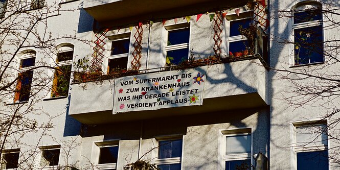 An einem Balkon hängt ein Plakat mit der Aufschrift: 