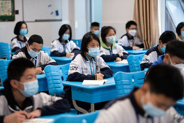 viele kinder sitzen in einem klassenzimmer mit maske