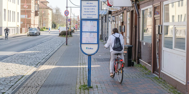Eine sportlich gekleidete Person fährt auf dem Rad an einer Bushaltestelle vorbei.
