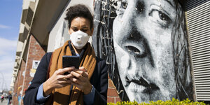 Eine Frau mit Mundschutz und Telefon vor einem Grafititi