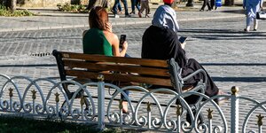 Zwei Frauen sitzen auf einer Bank in Istanbul und schauen auf ihre Smartphones