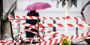 Absperrbänder vor einem Cafe, im Hintrgrund eine Frau mit Regenschirm
