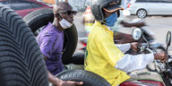 Zwei Männer sitzen auf einem Motorrad, der Fahrer mit, der Beifahrer mit Maske unterm Kinn
