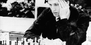 Ein schwarz-weiß Bild, darauf ein junger Mann, der vor einem Schachbrett sitzt und nachzudenken scheint.