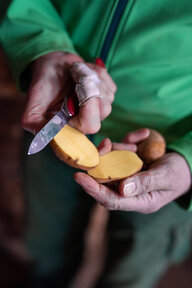 Hände halten ein Messer und eine aufgeschnittene Kartoffel