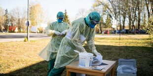 Zwei Menschen in Schutzkleidung stehen auf einer Wiese