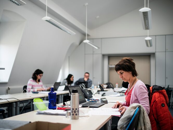 Mehrere Menschen sitzen an einem langen Tisch und blicken in ihre Unterlagen.