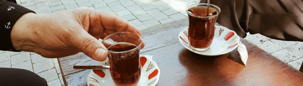 Zwei Menschen, von denen nur die Hände zu sehen sind, greifen nach ihren türkischen Teetassen aus Glas