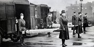 Rot-Kreuz-Frauen mit Atemschutzmasken während der Spanischen Grippe 1918 in St. Luis (Missouri). Sie tragen Bahren und hitner ihnen stehenHolzwagen zum Abtransport