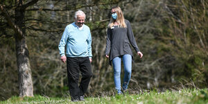 Ein älterer Mann geht mit einer Frau mit Atemschutzmaske in der Natur spazieren.