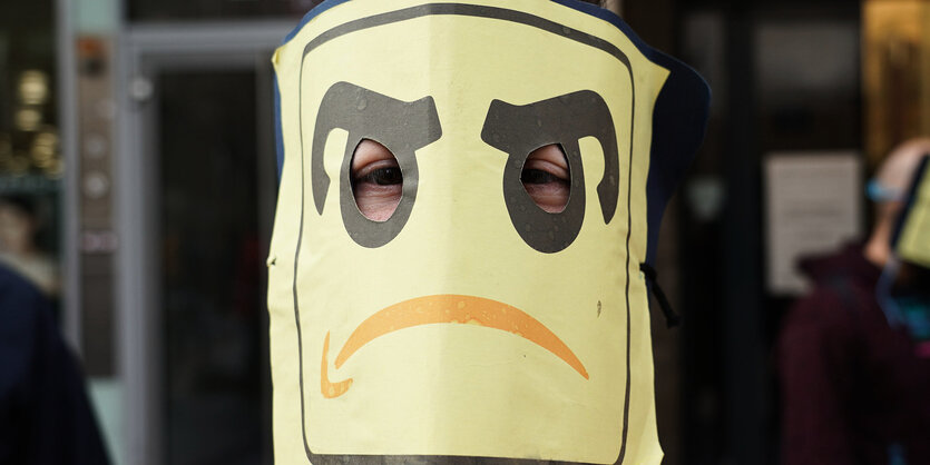 Ein Mann trägt eine Maske mit einem Amazonlogo das weint