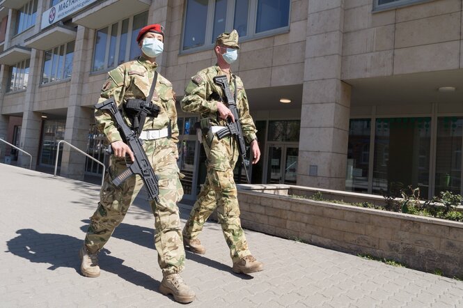 Zwei Soldaten mit Mundschutz und Waffen laufen eine Straße lang