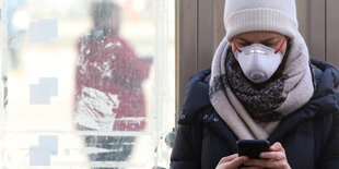 Eine Frau mit Atemmaske schaut auf ihr Smartphone