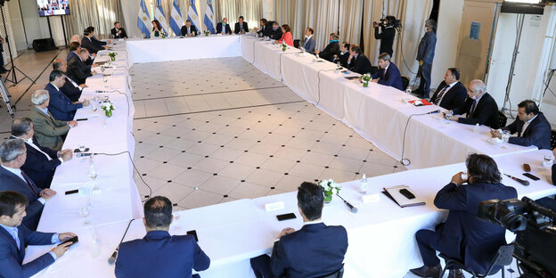 Um einen Tisch herum versammelt sitzen zahlreiche Vertreter der argentinischen Regierung