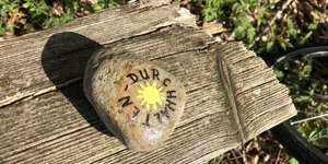 Ein Stein auf den eine Sonne und das Wort "Durchhalten" gemalt sind.