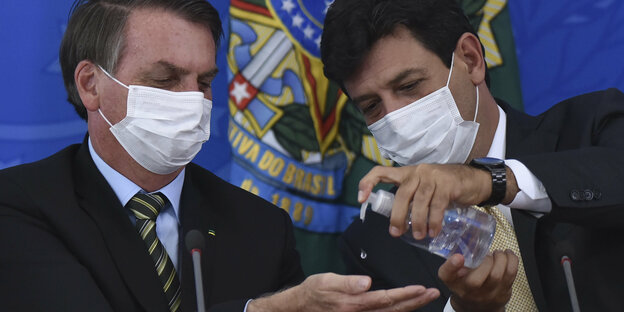 Luiz Henrique Mandetta desinfeziert Bolsonaros Hände mti einem Spender. Beide tragen Mundschutz Masken