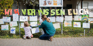 Eine Mutter befestigt mit ihrer Tochter ein selbstgemaltes Bild am Zaun eines geschlossenen Kindergartens i