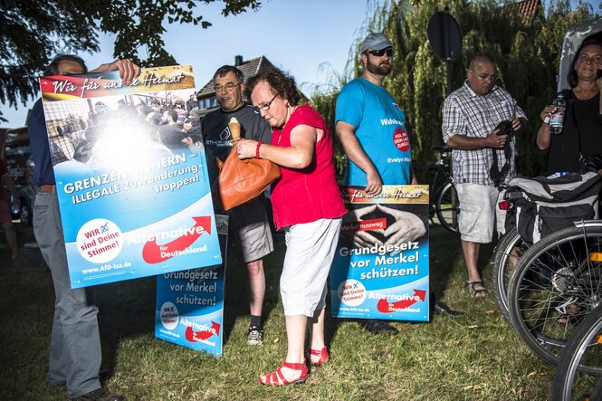 AFD Anhänger stehen mit Protestplakaten gegen Merkel auf einer Wiese