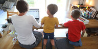 Von hinten ist eine Mutter zu sehen, die am Laptop arbeitet, neben ihr zwei Kinder