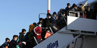 Viele Kinder mit Mundschutz auf einer Gangway zu einem Flugzeug