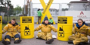 Gelb gekelidete Greenpeace-Aktivisten sitzen neben gelben Tonnen vor der Brennelementefabrik Linen